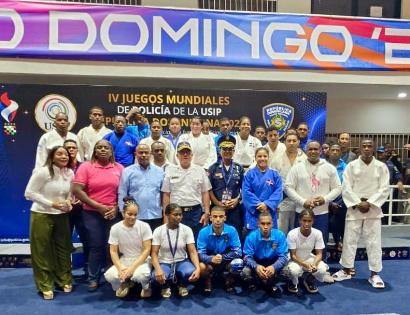 Judocas y representantes dominicanos posan ante el fondo de los IV Juegos Mundiales de Policía, algunos con sus medallas.