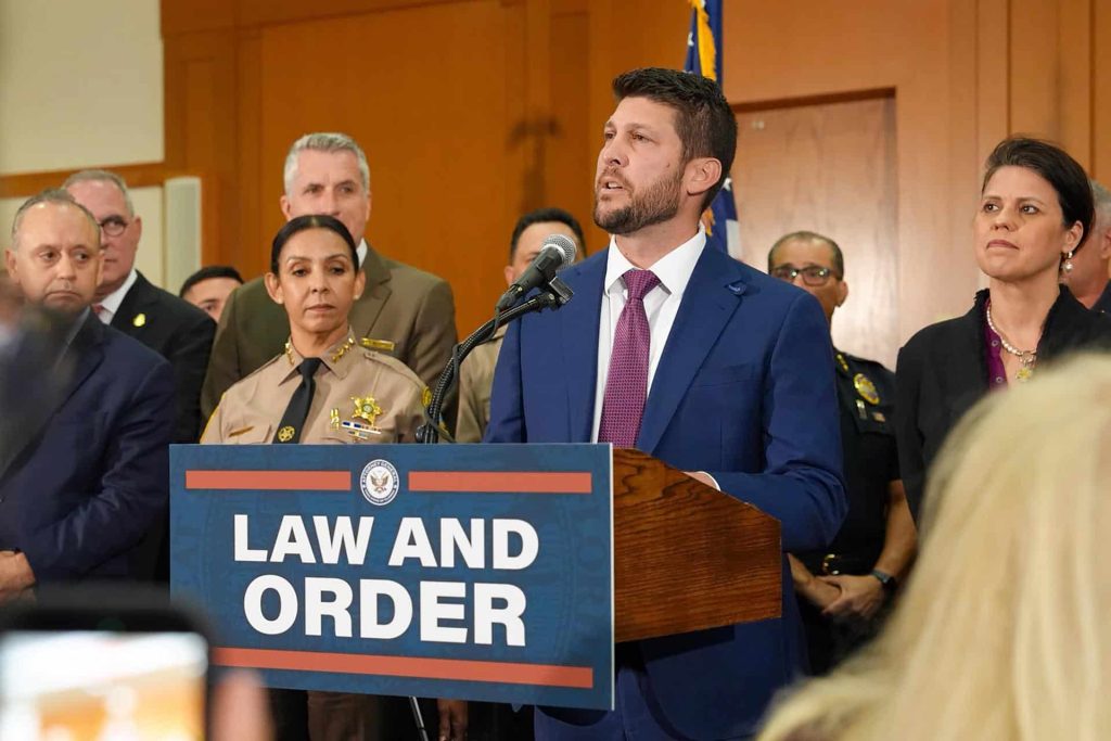 Un hombre habla ante un atril con el letrero LAW AND ORDER, acompañado por varias personas