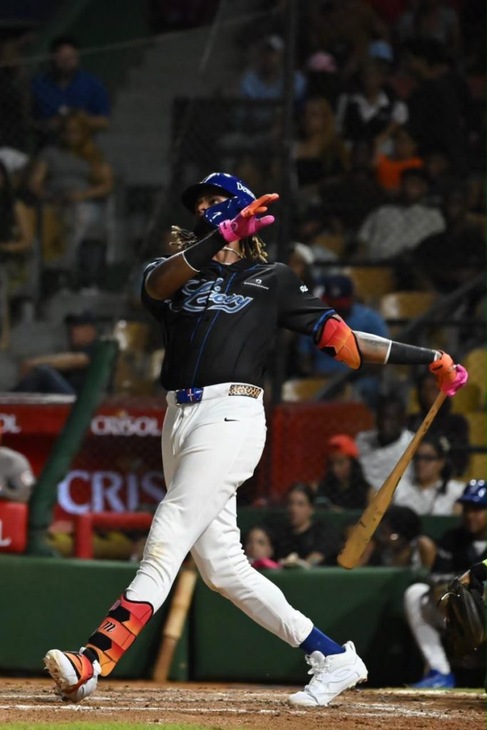 Kevin Alcántara sigue la trayectoria de la pelota con el bate en una mano y uniforme del Licey