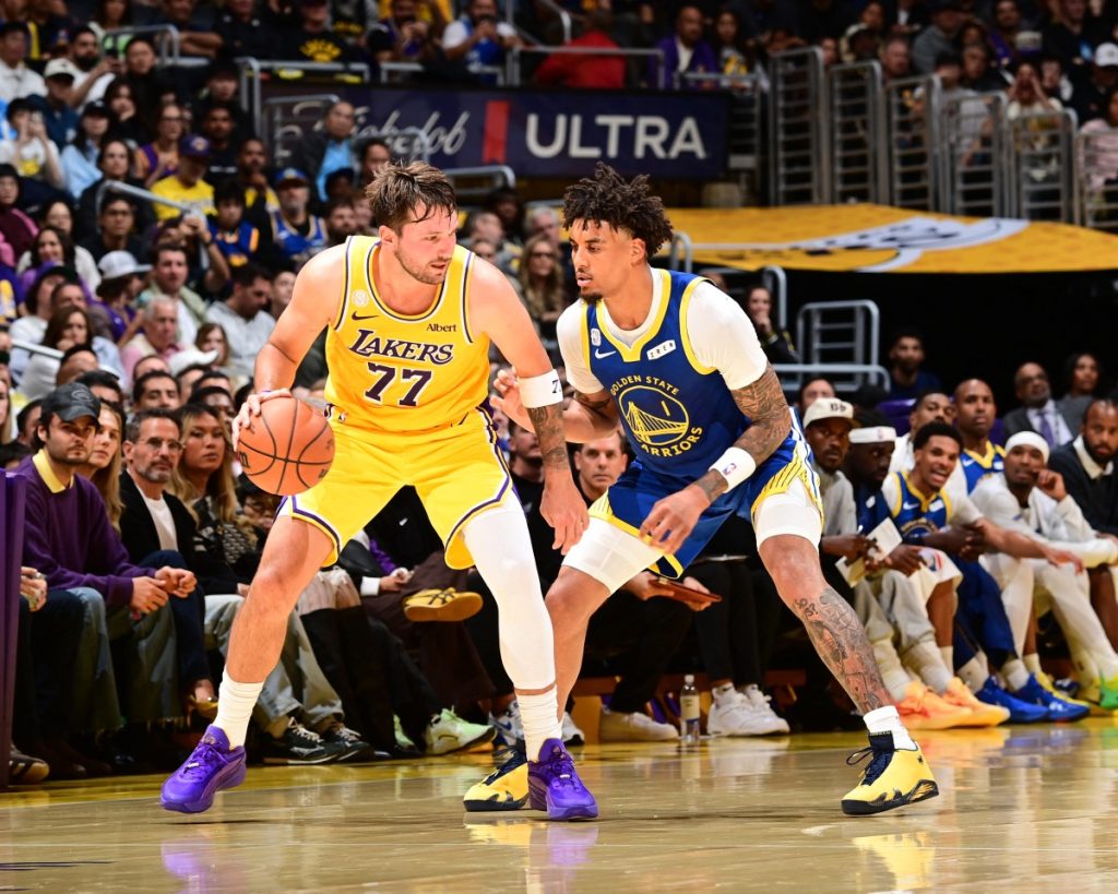 Jugador de los Lakers con el balón frente a un defensor de los Warriors durante un partido de baloncesto.