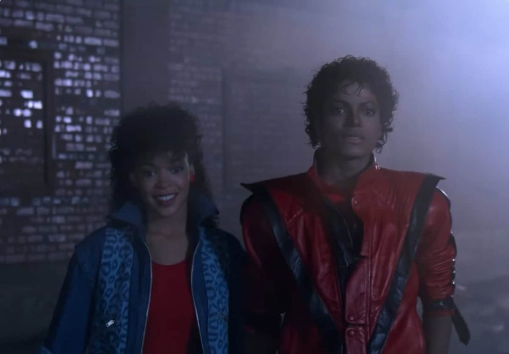 Michael Jackson con una chaqueta roja y negra junto a una mujer en el video Thriller.